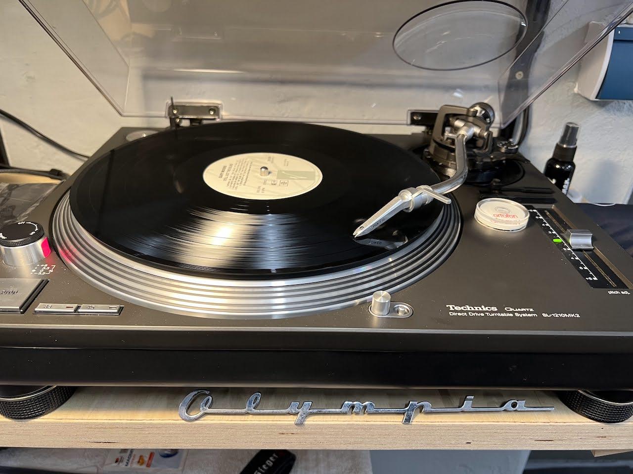 A Technics SL 1210 MK2 spinning "Garry more Still got the Blues", in front a Olympia badge from an old Opel, some maintanance Stuff at the side